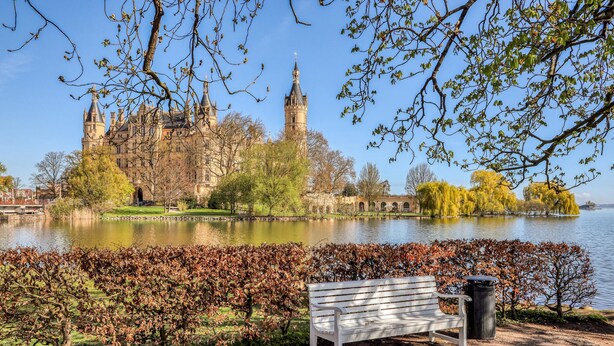 A park with a bench, a body of water, and a historic building with towers in the background. - Stunning home in Schwerin with WiFi (Schwerin)