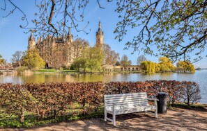 Ein Park mit einer Bank, einem Gewässer und einem historischen Gebäude mit Türmen im Hintergrund.