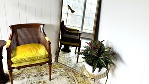 Ein Zimmer mit einem Holzstuhl mit gelber Sitzkissen, einem großen Spiegel und einer Topfpflanze.