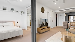 Een moderne slaapkamer met een bed, nachtkastjes, een televisie en een grote spiegel.