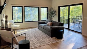 A spacious living room with a large window, a sofa, a chair, and a small table. - Villa 1 on Preserve Golf Course! (Pequot Lakes)