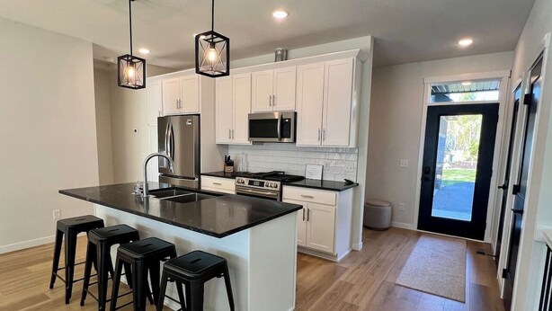 A modern kitchen with a central island, white cabinets, stainless steel appliances, and black bar stools. - Villa 1 on Preserve Golf Course! (Pequot Lakes)