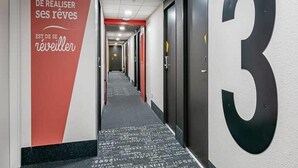 A hotel corridor with a red wall featuring text, a black carpet with white text, and a large black number '3' on the wall. - B&B Hotel Bordeaux Sud Mios (Mios)