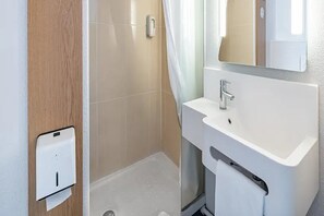 Une salle de bain avec un lavabo blanc, un miroir et un espace douche.