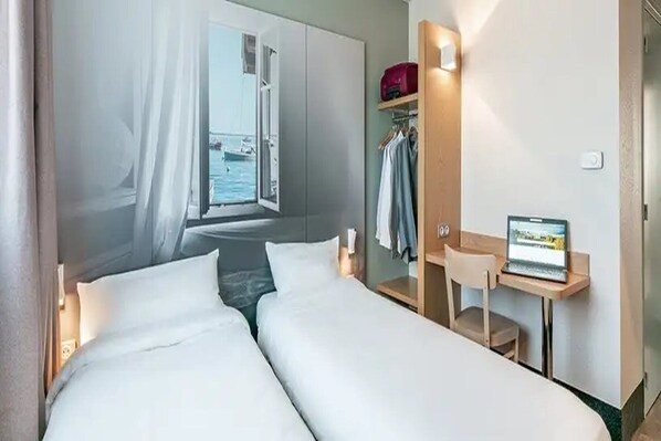 A hotel room with two beds, a desk with a laptop, a wardrobe, and a view of the sea. - B&B Hotel Bordeaux Sud Mios (Mios)