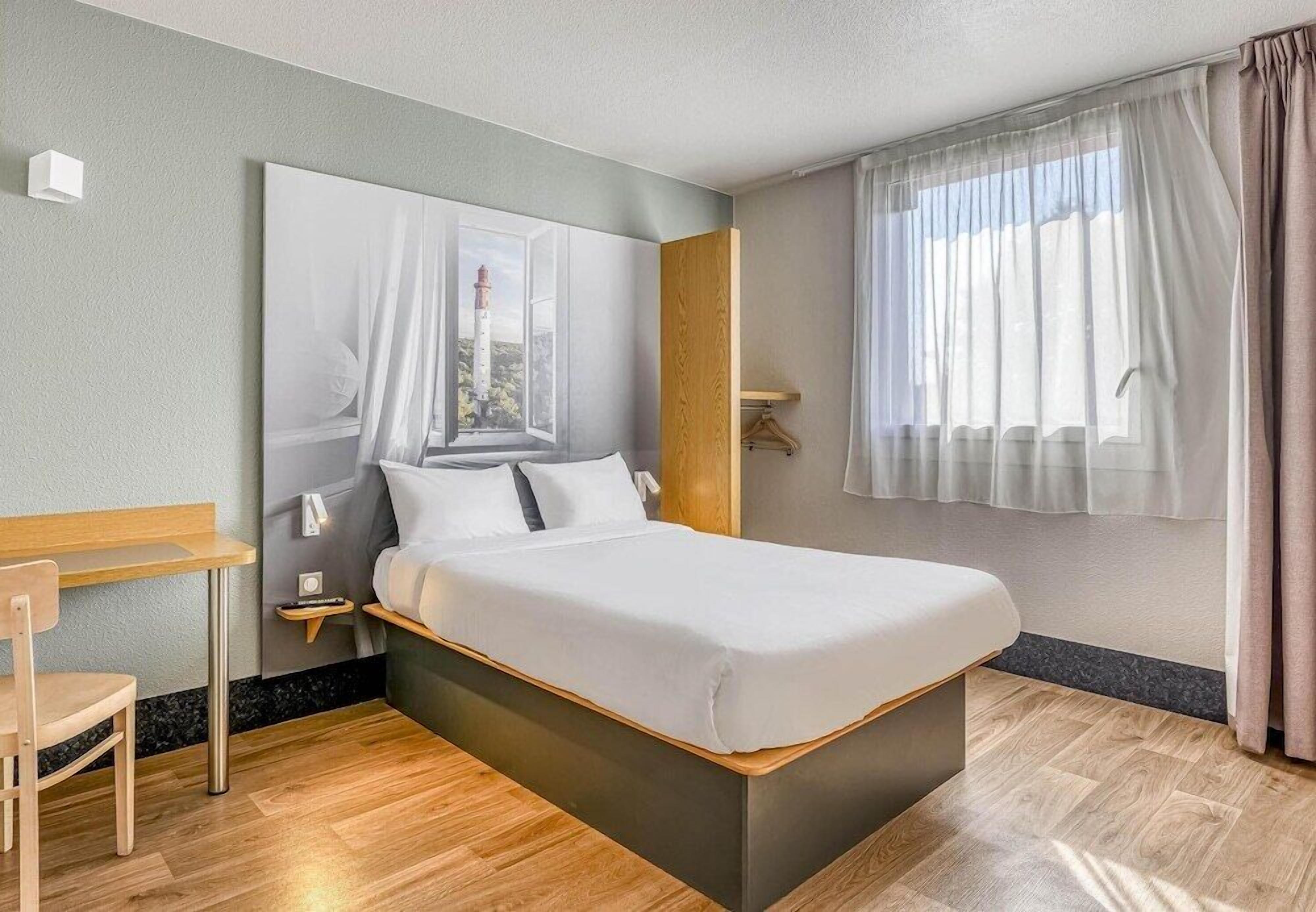 Ein modernes Hotelzimmer mit Bett, Schreibtisch und Blick auf einen Leuchtturm durch ein Fenster.