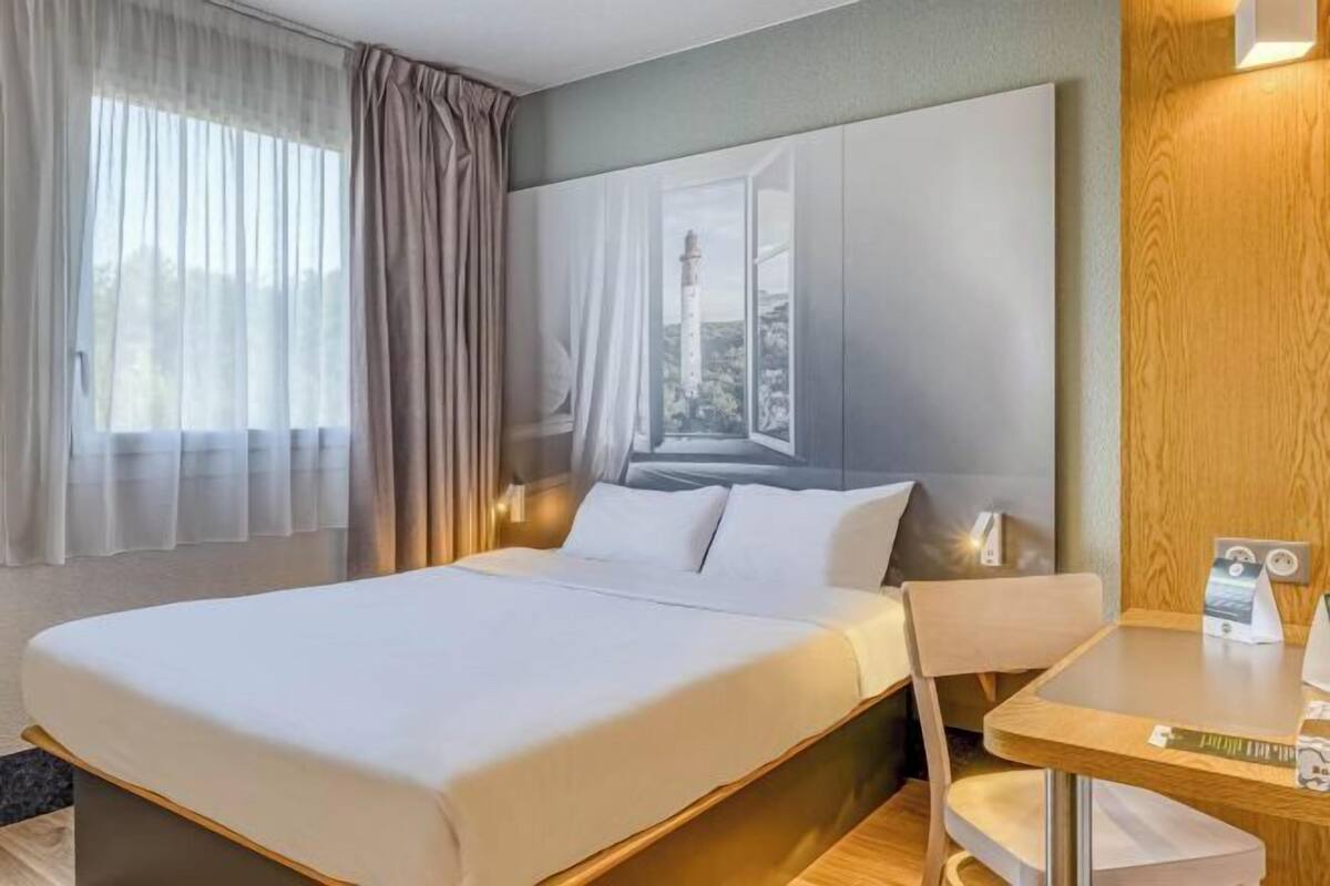 Een hotelkamer met een groot bed, een houten bureau en uitzicht op een vuurtoren door een raam.
