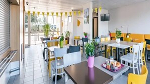 A modern dining area with yellow and white chairs, tables, and potted plants. - B&B Hotel Bordeaux Sud Mios (Mios)