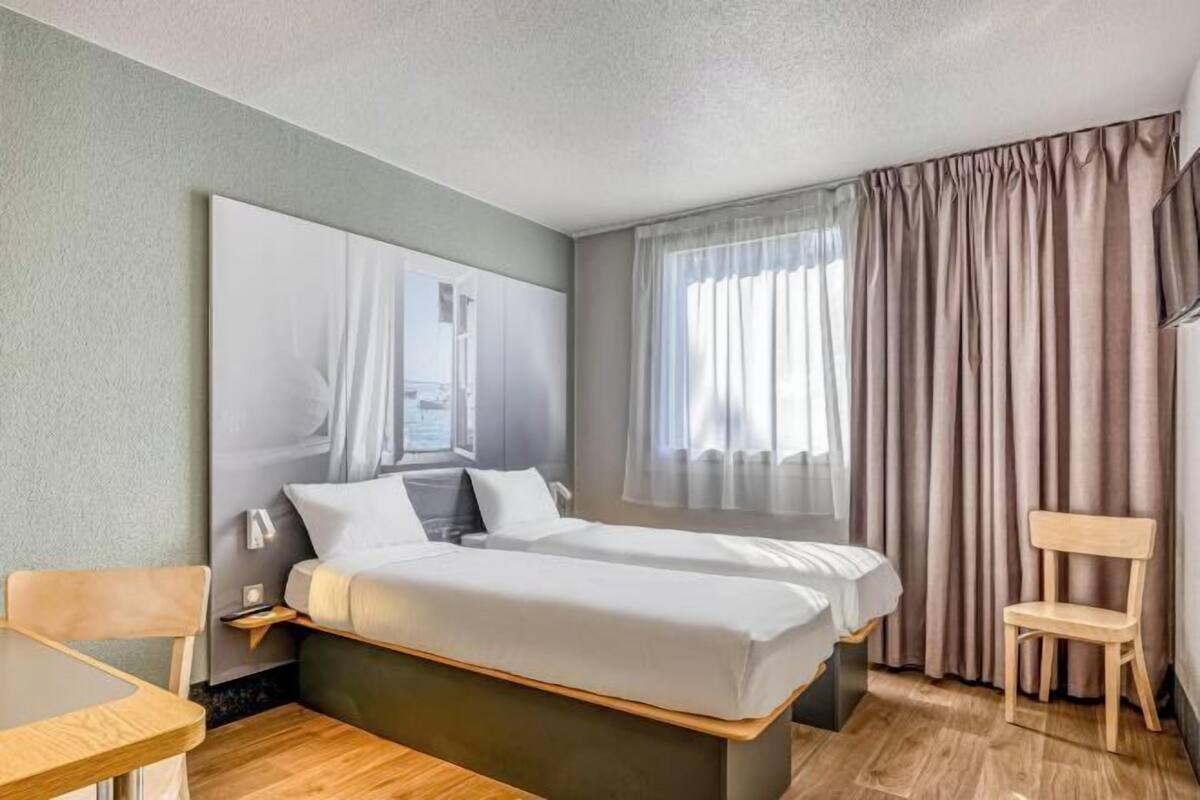 Een hotelkamer met een bed, een bureau, een stoel en een groot raam met gordijnen.