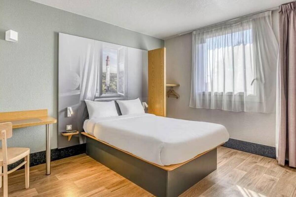 Een moderne hotelkamer met een groot bed, een houten bureau en een raam met dunne gordijnen.