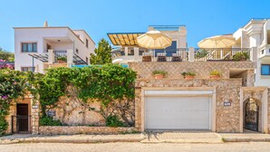 Un bâtiment moderne avec une façade en pierre, une porte de garage et des plantes en pot sur le balcon.
