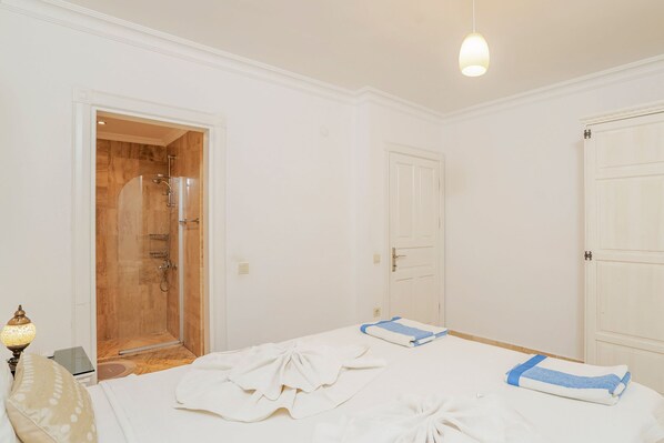 A bedroom with a wooden door, a white bed with a blue blanket, and a lamp on the left. - Villa Vanilla in Kalkan (Kaş)