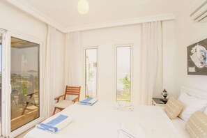A hotel room with a large bed, a chair, a table, and a view of the outdoors. - Villa Vanilla in Kalkan (Kaş)