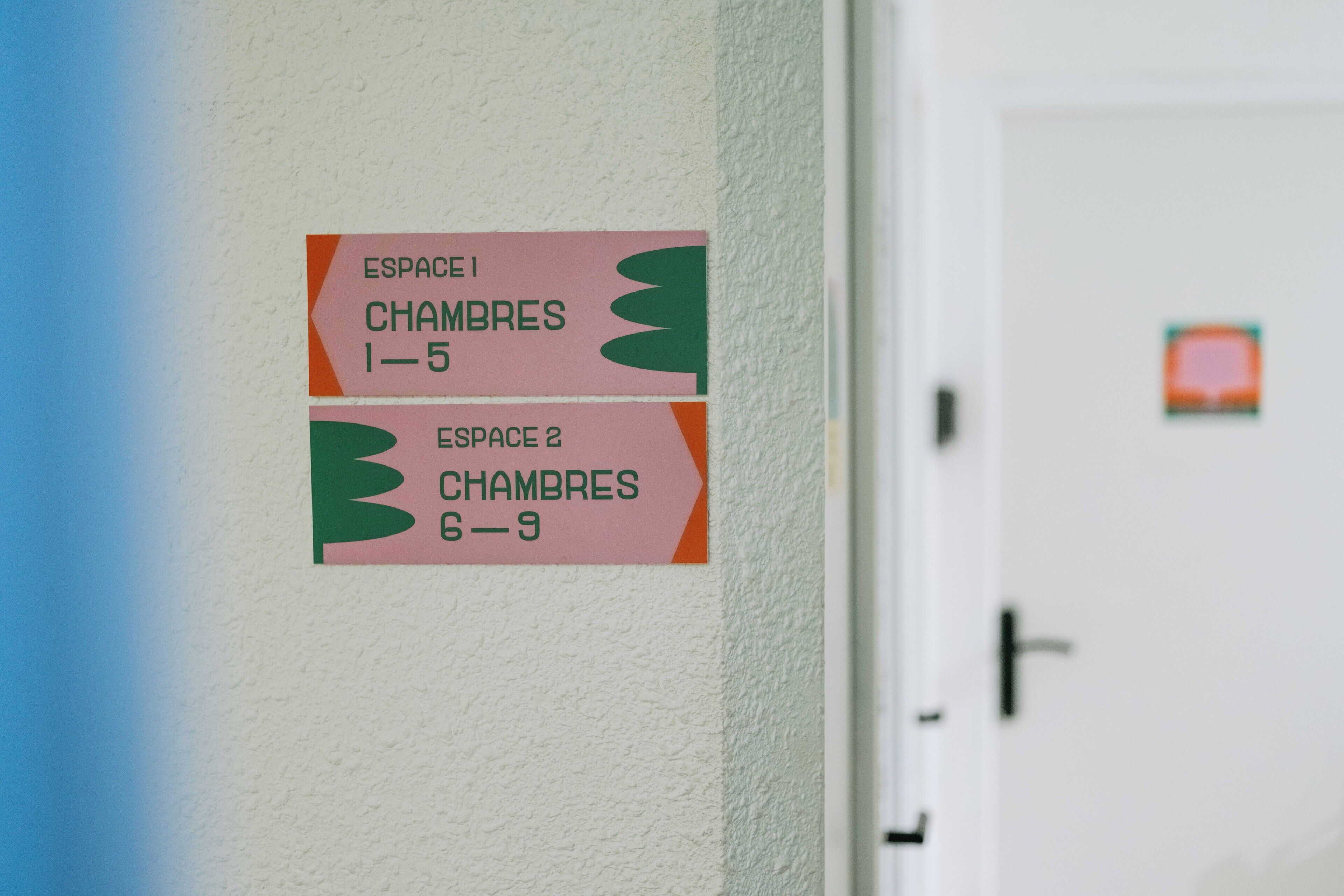 Deux panneaux sur un mur indiquant les numéros et les noms des salles : « ESPACE 1 – 5 CHAMBRES » et « ESPACE 2 – 9 CHAMBRES ».