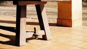 A wooden bench with a metal support structure, positioned on a tiled patio with a natural backdrop of trees. - La Donaclaudré - Large 63-person group gîte in the heart of nature, 1 hour from Paris. (Saint-Augustin)