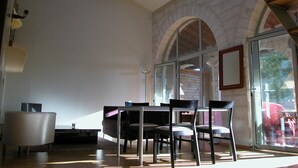 A spacious room with a dining table and chairs, a modern chandelier, and a stone wall with arched windows.