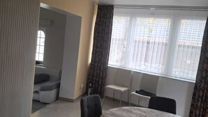 Ein geräumiges Zimmer mit einem runden Tisch und Stühlen, einem Sofa und einem Fenster mit Vorhängen.