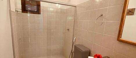 A bathroom with a glass-enclosed shower, a toilet, and a towel rack with a red flower.