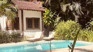 A poolside area with a white building, a tiled roof, and a pool. - Big Bambu (Porto Seguro)