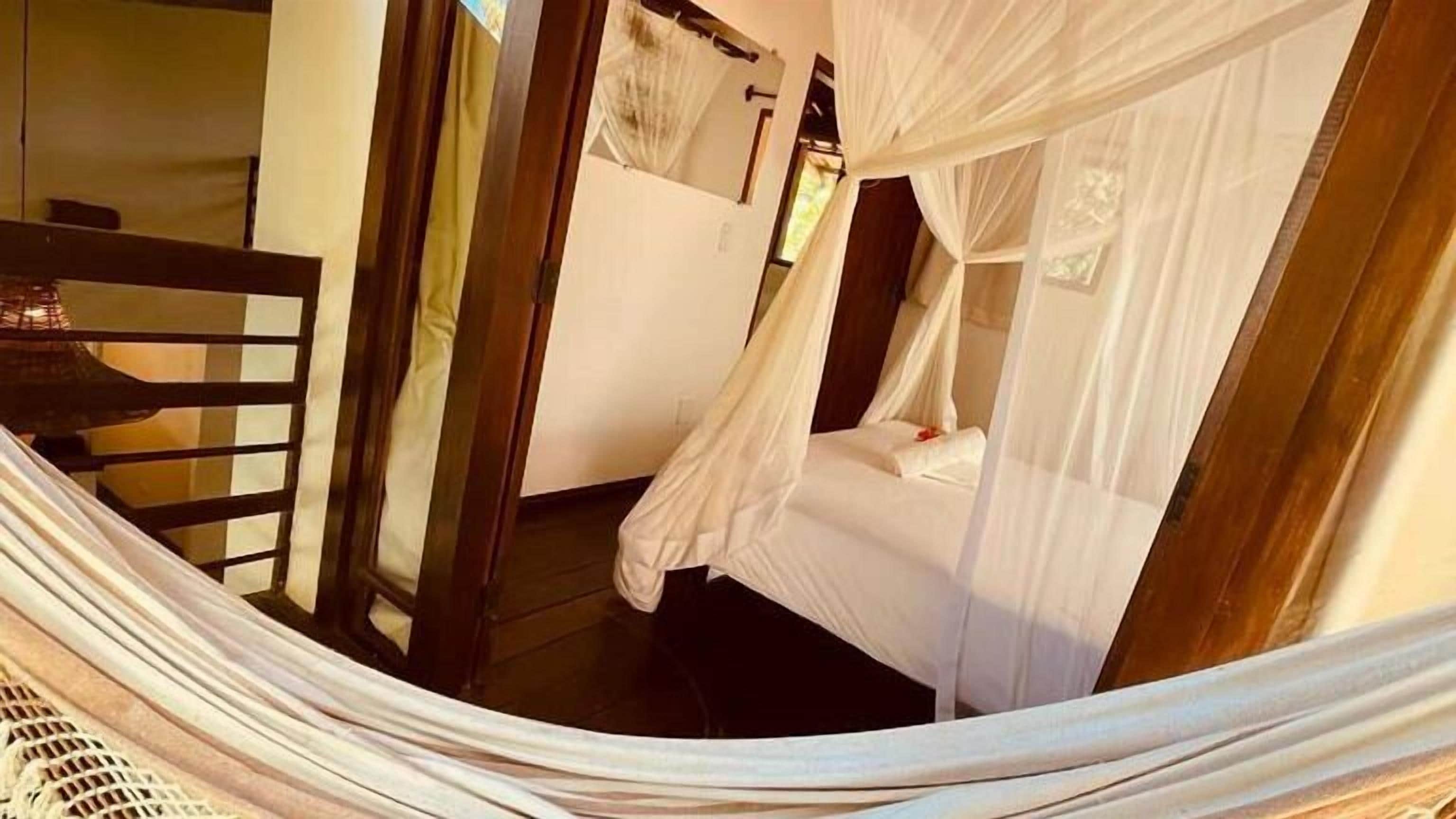 Een kamer met een bed dat overdekt is door een witte hemel, een houten deur en een raam met gordijnen.