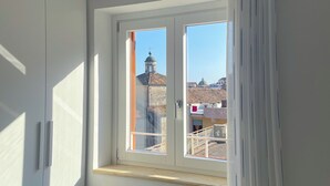 Ett rum med ett stort fönster, en garderob och utsikt över byggnaderna utanför.