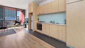 A modern kitchen with wooden cabinets, a built-in oven, and a large window overlooking a cityscape. - Chic Apartment in Heart of Adelaide (Adelaide)