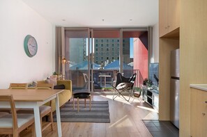 A modern living room with a dining area, a sofa, a chair, and a table. There is a large window with a view of buildings outside. - Chic Apartment in Heart of Adelaide (Adelaide)