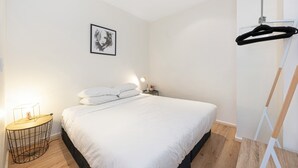 A bedroom with a bed, a bedside table with a lamp, a framed picture on the wall, and a coat rack. - Chic Apartment in Heart of Adelaide (Adelaide)