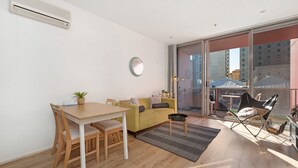 A modern living room with a dining area, a yellow sofa, a round mirror, and a large window with a view of buildings. - Chic Apartment in Heart of Adelaide (Adelaide)