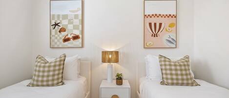 A hotel room with two beds, a nightstand with a lamp, and two wall-mounted artworks.