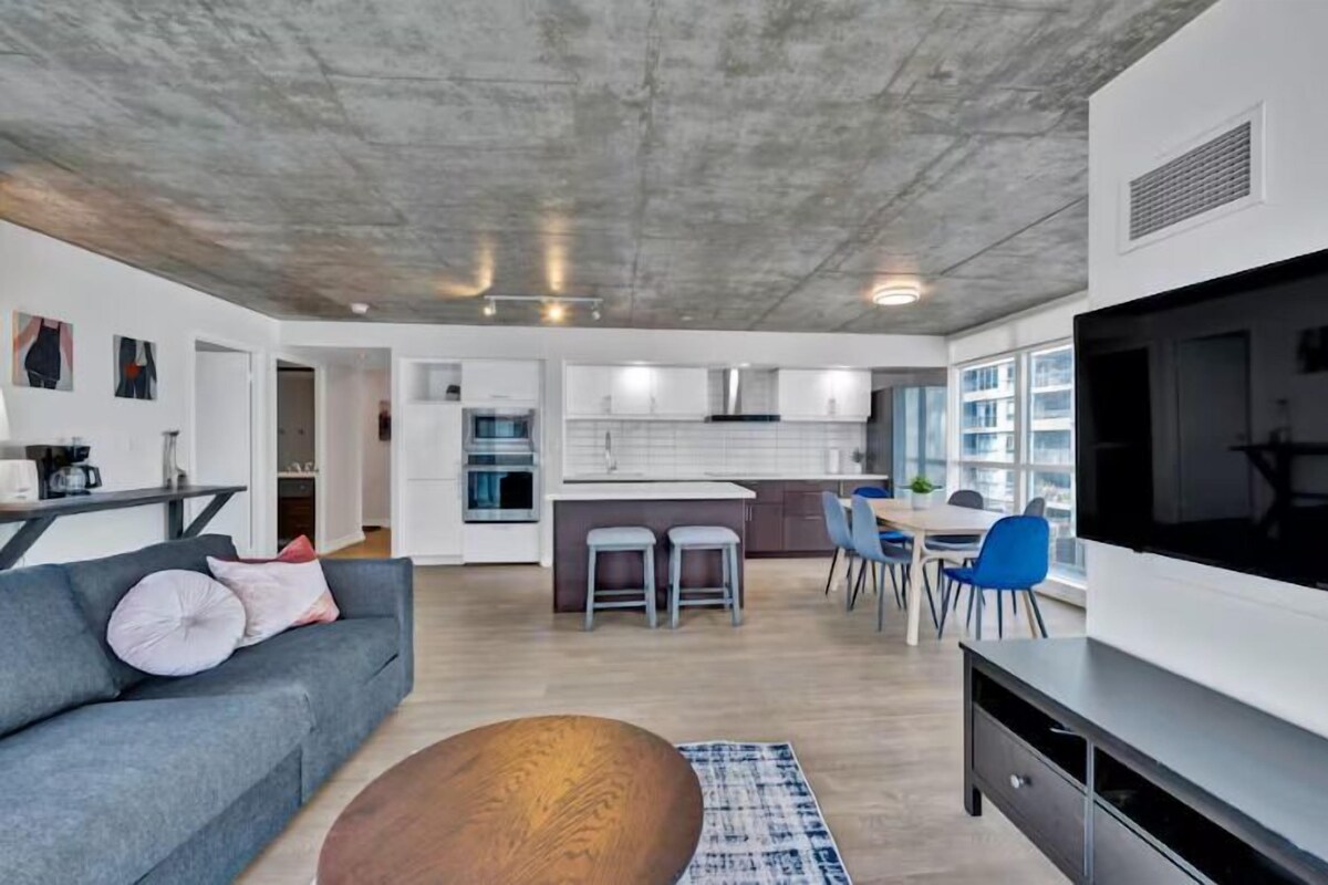 A modern apartment with a living room, kitchen, dining area, and a large TV.