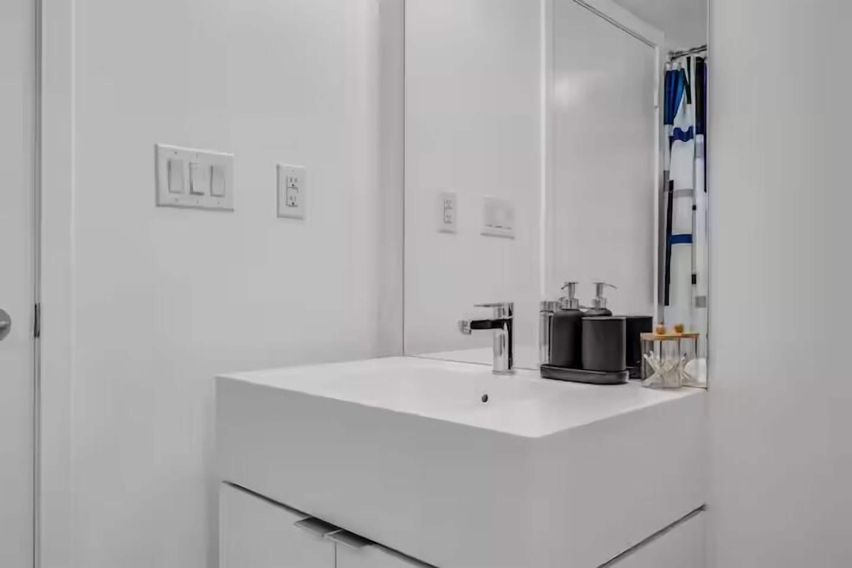 A modern bathroom with a white sink, a mirror, and a shower curtain.
