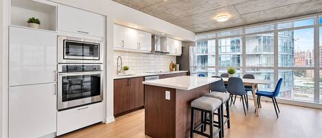 A modern kitchen with built-in appliances, a central island, and a dining area with chairs.