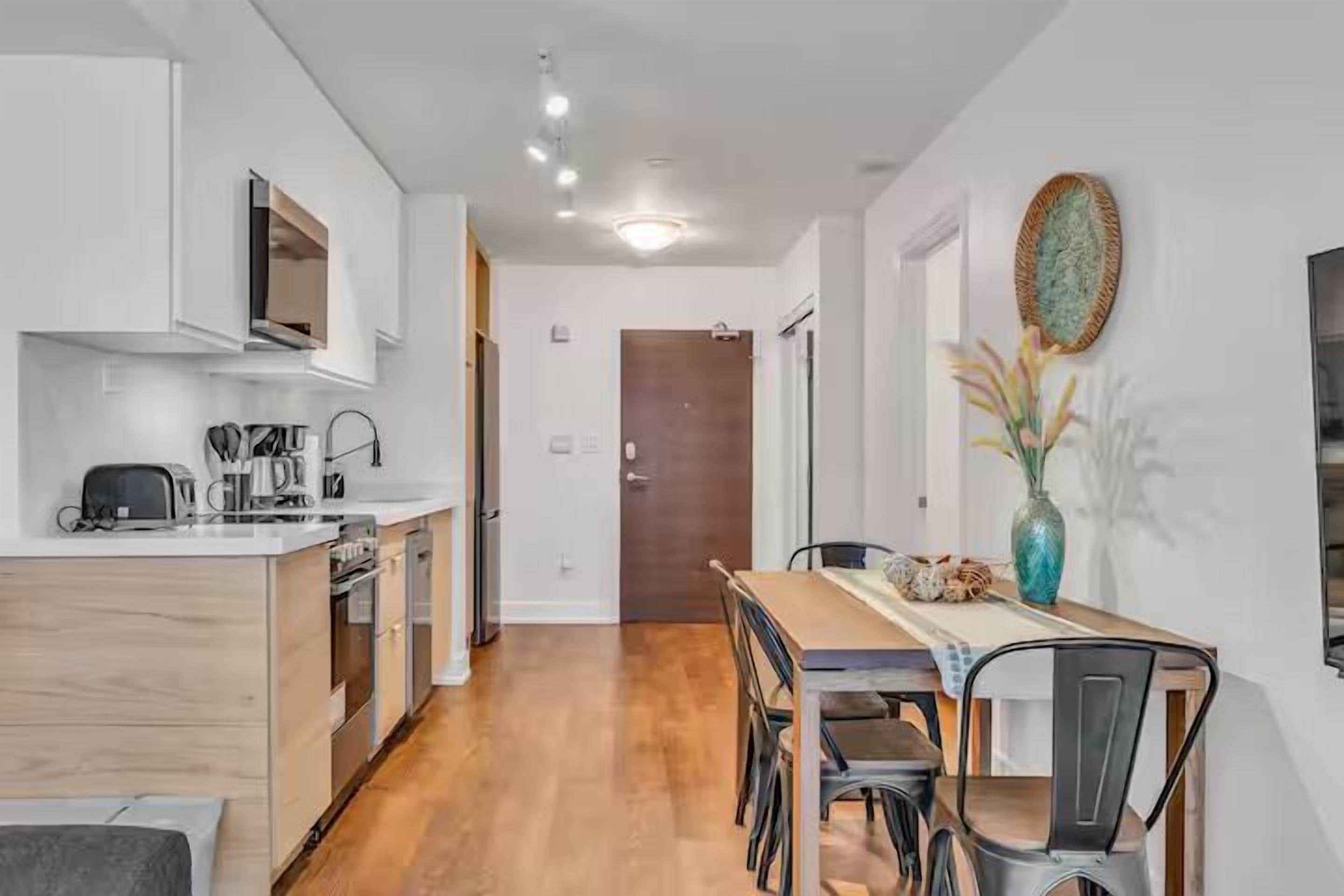 Una cocina moderna con armarios de madera, una mesa de comedor con sillas y un jarrón decorativo en la pared.