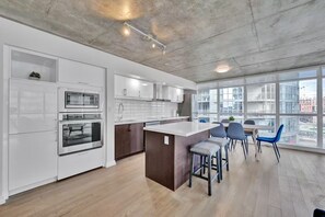 A modern kitchen with white cabinetry, a central island, and a dining area with chairs. - HostlyStays Luxury Suites  (Toronto)