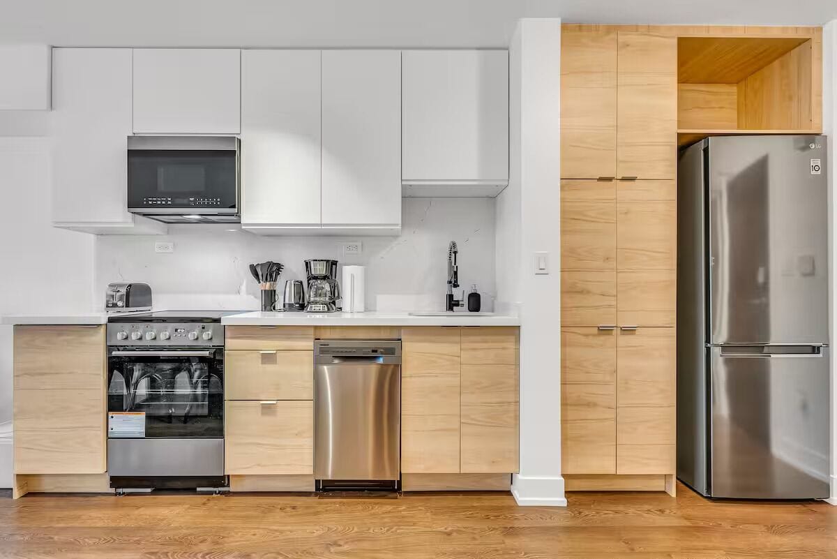 A modern kitchen with white cabinets, stainless steel appliances, and a wooden floor.