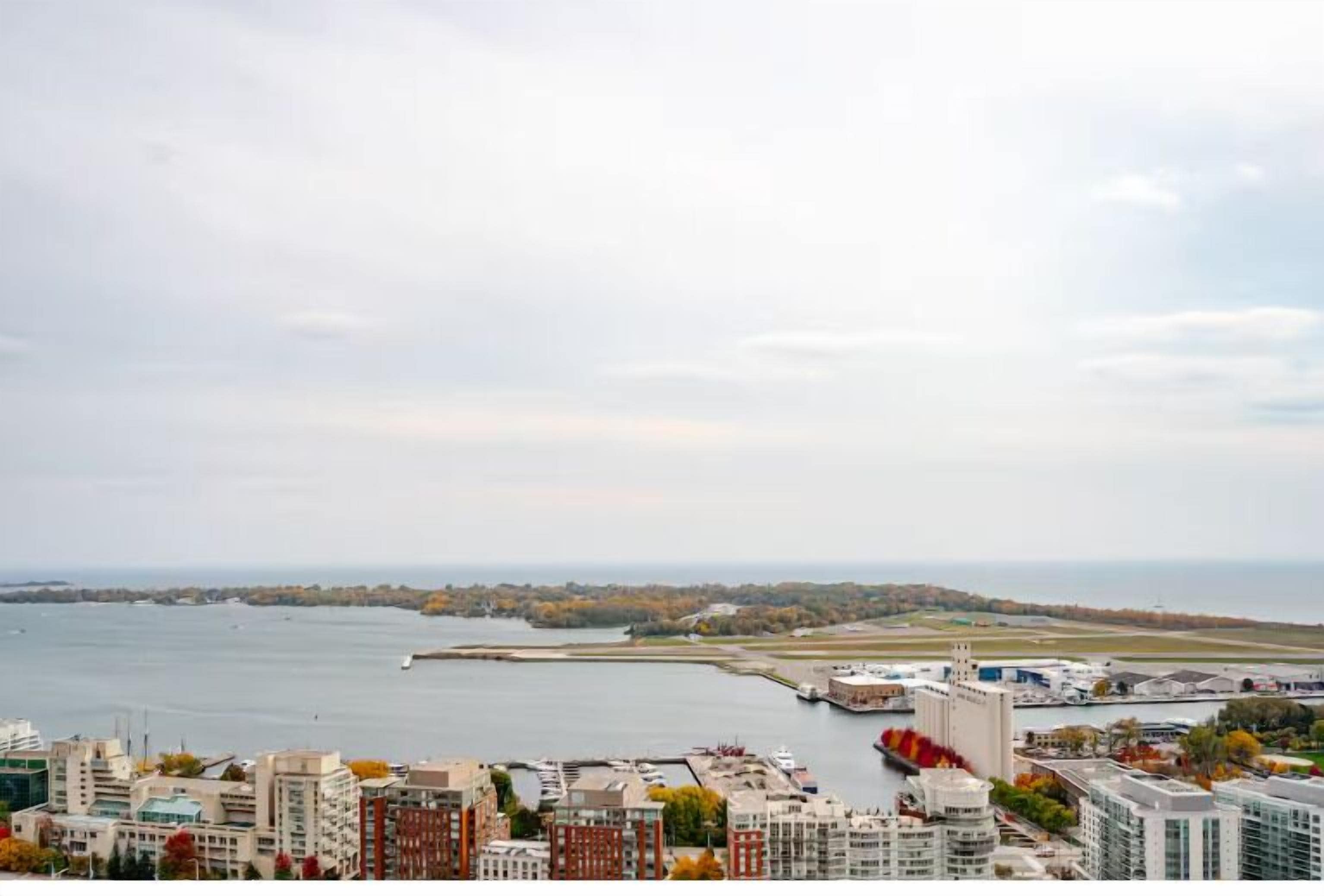 A coastal cityscape with modern buildings, a marina, and a distant shoreline.