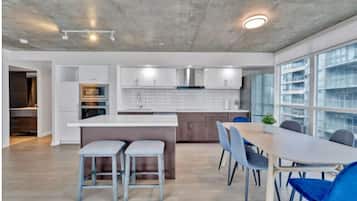 Et moderne køkken med hvide skabe, en central ø og et spiseområde med blå stole.