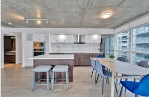 A modern kitchen with white cabinets, a central island, and a dining area with blue chairs. - HostlyStays Luxury Suites  (Toronto)