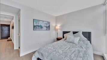 A bedroom with a large bed, a nightstand, a wall-mounted lamp, and a painting.