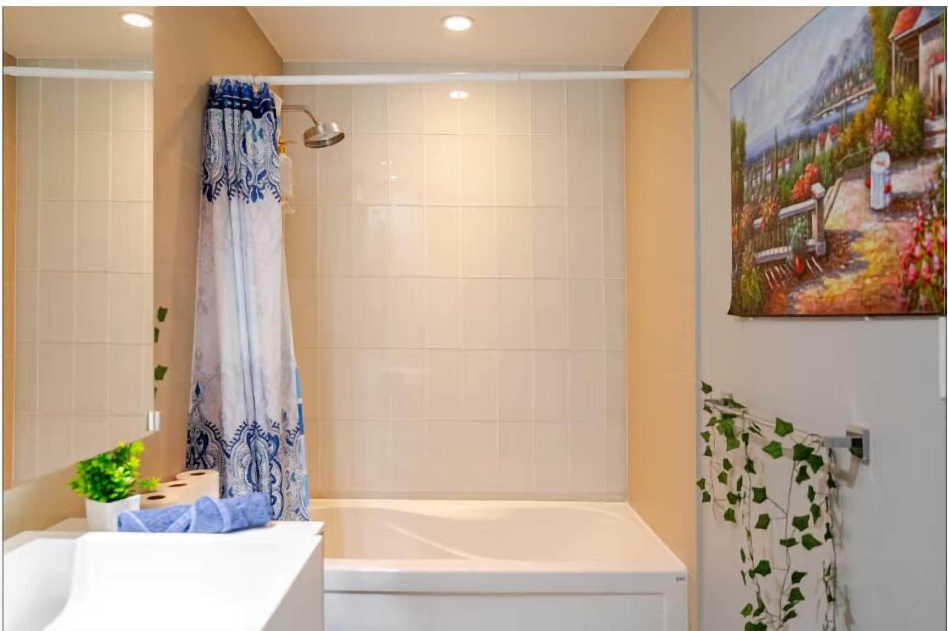 A bathroom with a shower, a bathtub, and a toilet. There is a towel rack with a towel and a potted plant on the counter.