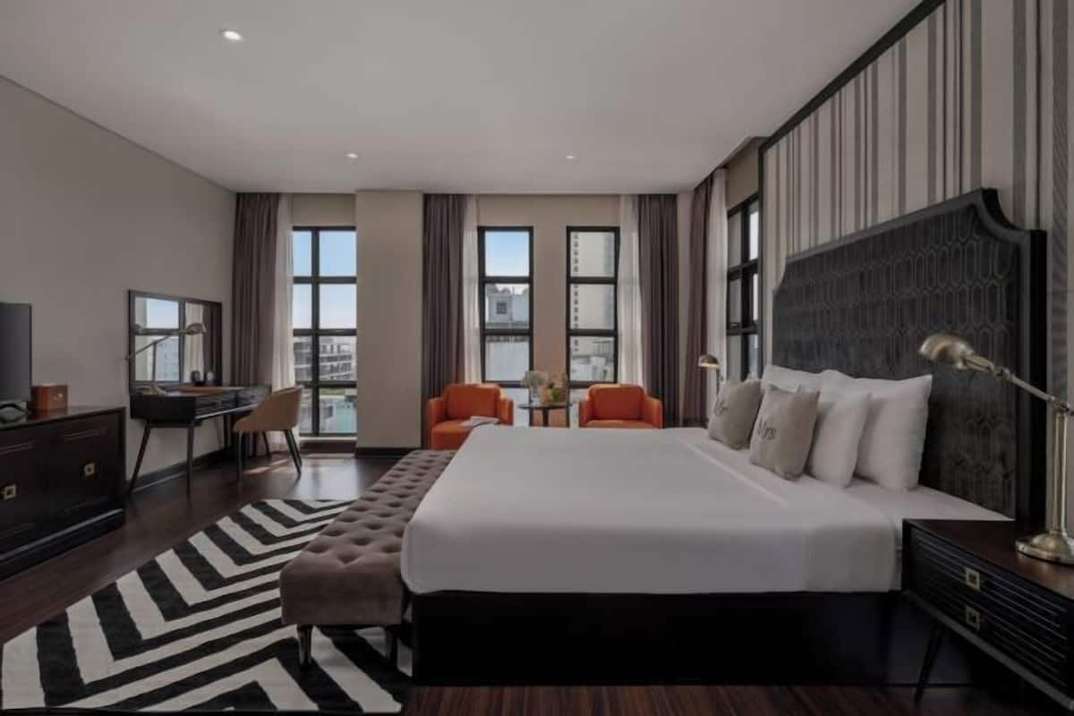 Ein modernes Hotelzimmer mit einem großen Bett, zwei Sesseln, einem Schreibtisch und einem Fernseher.