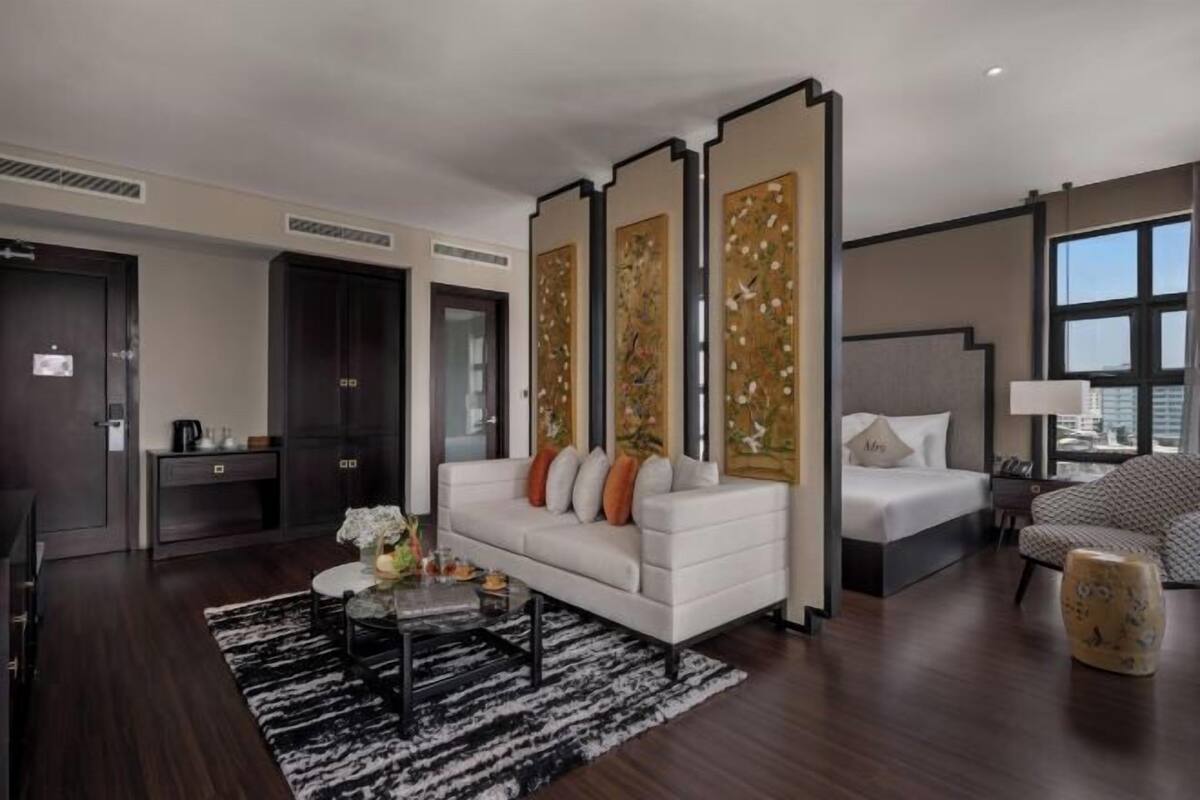 Ein modernes Hotelzimmer mit einem weißen Sofa, einem Bett, einem Schreibtisch und einem großen Fenster.