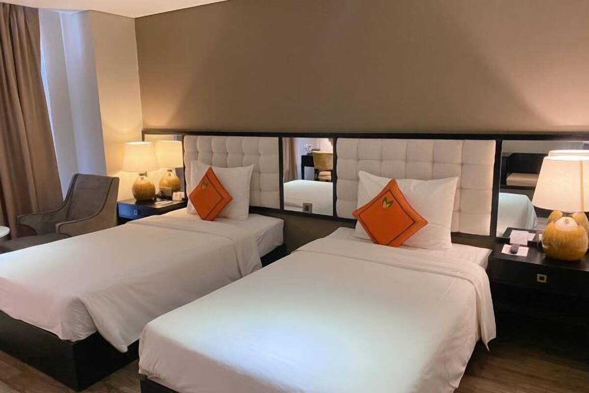 Ein Hotelzimmer mit zwei Betten, einem Nachttisch mit Lampe, einem Sessel und einem großen Spiegel an der Wand.