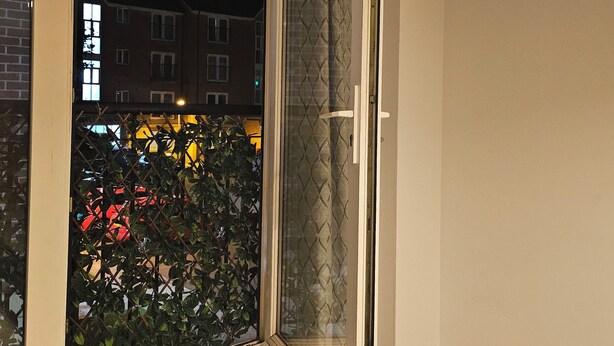 Una habitación con puerta corrediza de vidrio que da a un balcón, suelo de baldosas y ventana con vistas a edificios y coches.