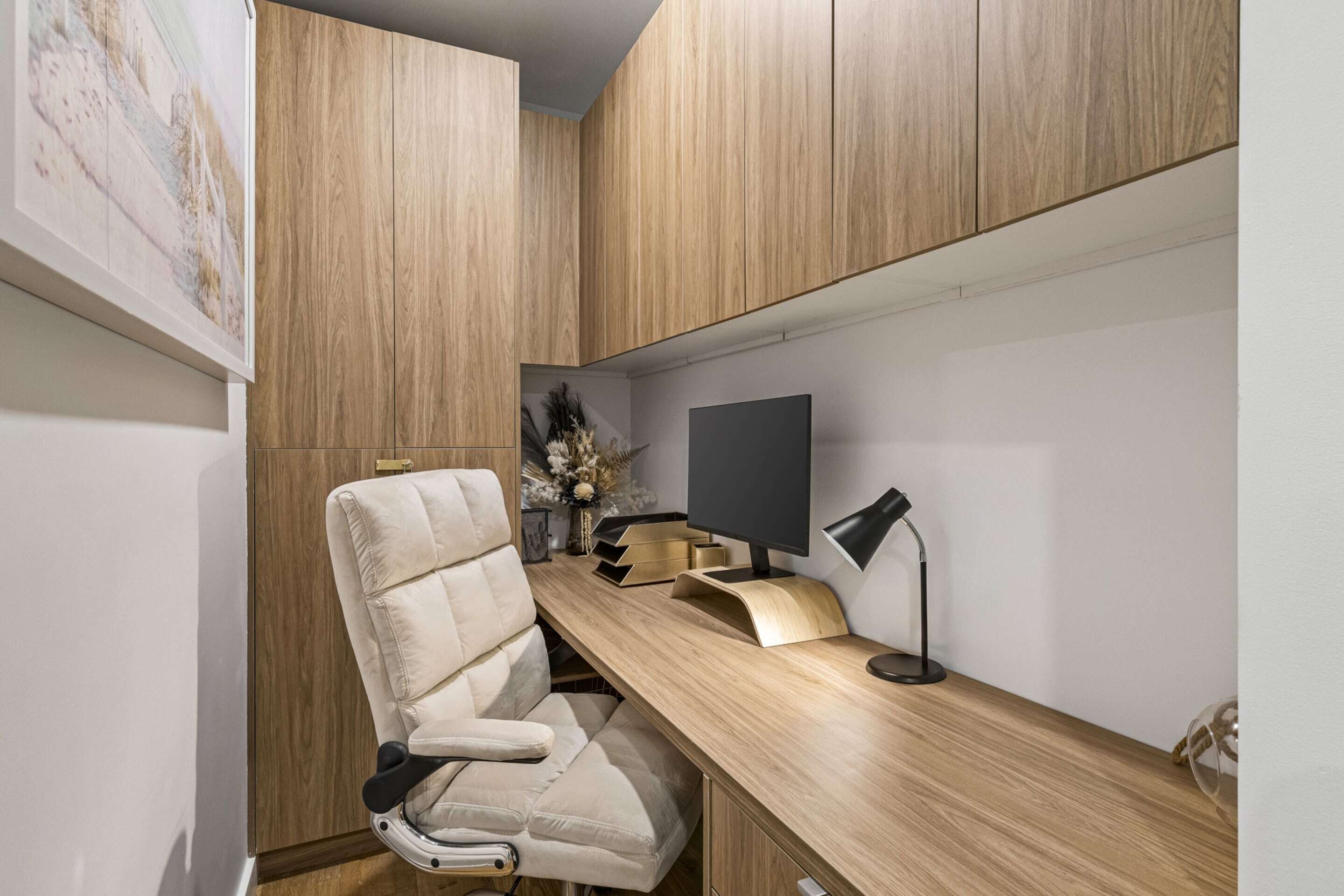 A modern office space with a wooden desk, a cushioned chair, a computer monitor, and a desk lamp.