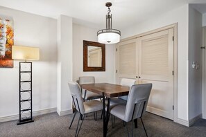 A dining area with a wooden table and four chairs, a floor lamp, a mirror, and a door with louvered panels. - Falcon Point 1BR/1Bath Sleeps 4 (Avon)