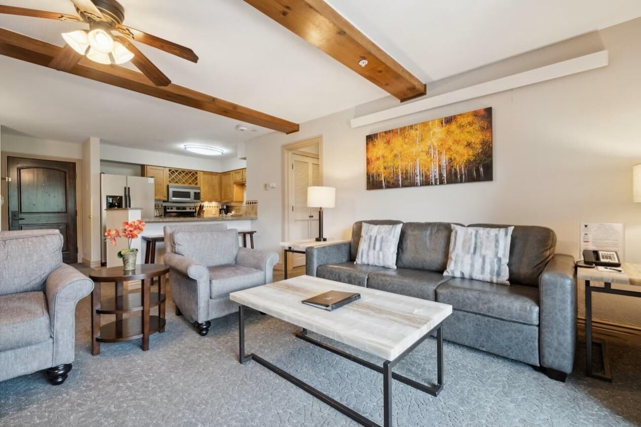 Un salon avec un canapé, des fauteuils, une table basse et un tableau au mur.