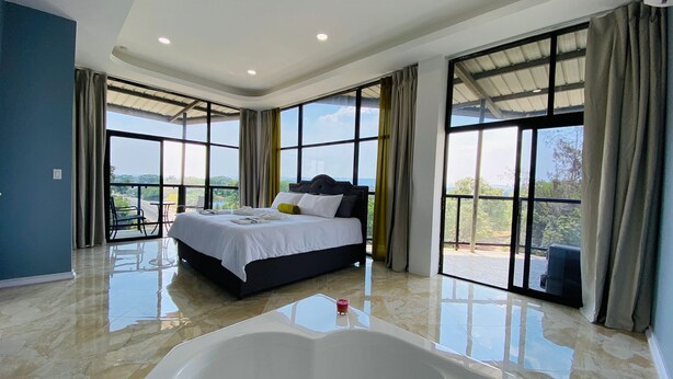 A spacious bedroom with a large bed, a bathtub, and large windows offering a view of the outdoors. - The Alexandria Marquis Hotel & Resorts (San Ignacio)