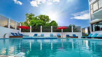 Una piscina al aire libre, sombrillas, sillones reclinables de piscina